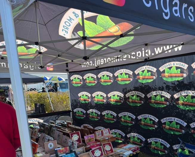 Interior view of a custom printed canopy tent for Cigars & More at a New Jersey outdoor event, featuring branded roof panels, a logo backdrop wall, and tables filled with cigar boxes and display products.
