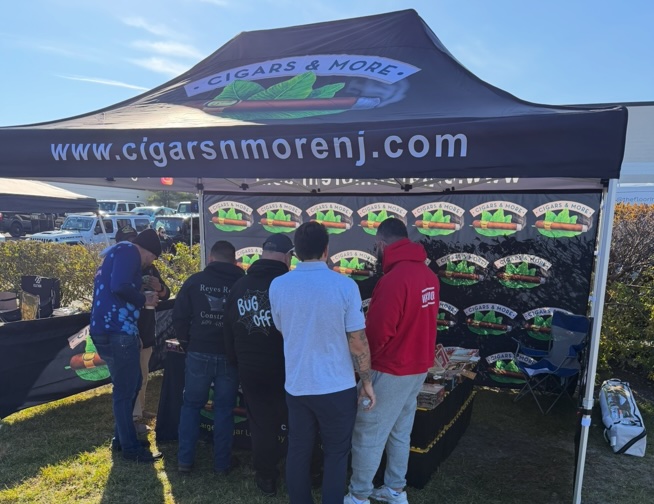 Black custom printed canopy tent for Cigars & More with logo and website displayed, set up at a New Jersey outdoor event with several customers gathered around a branded table and backdrop near the waterfront.